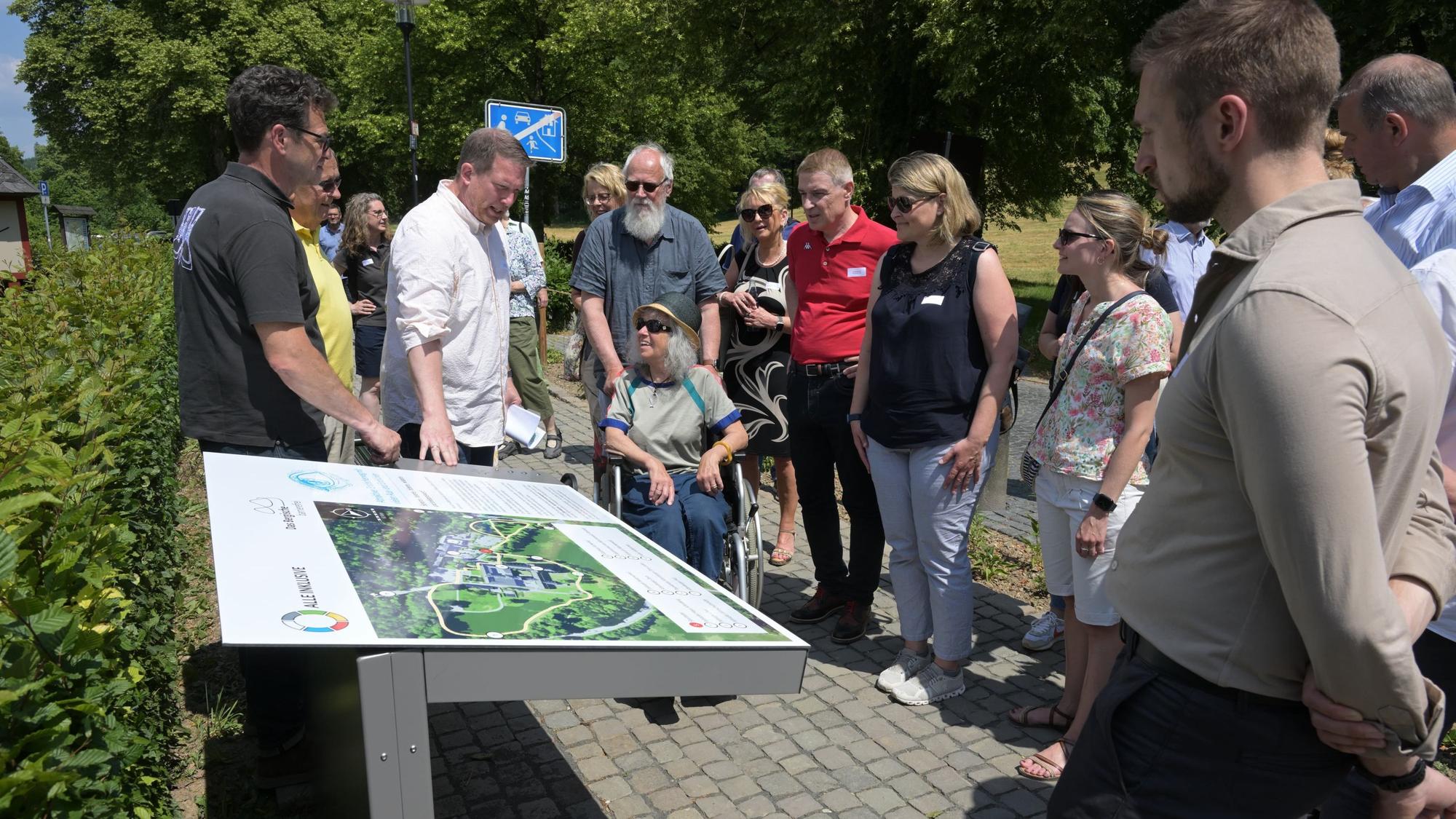 Menschen im Rollstuhl und ohne blicken auf eine Infotafel.