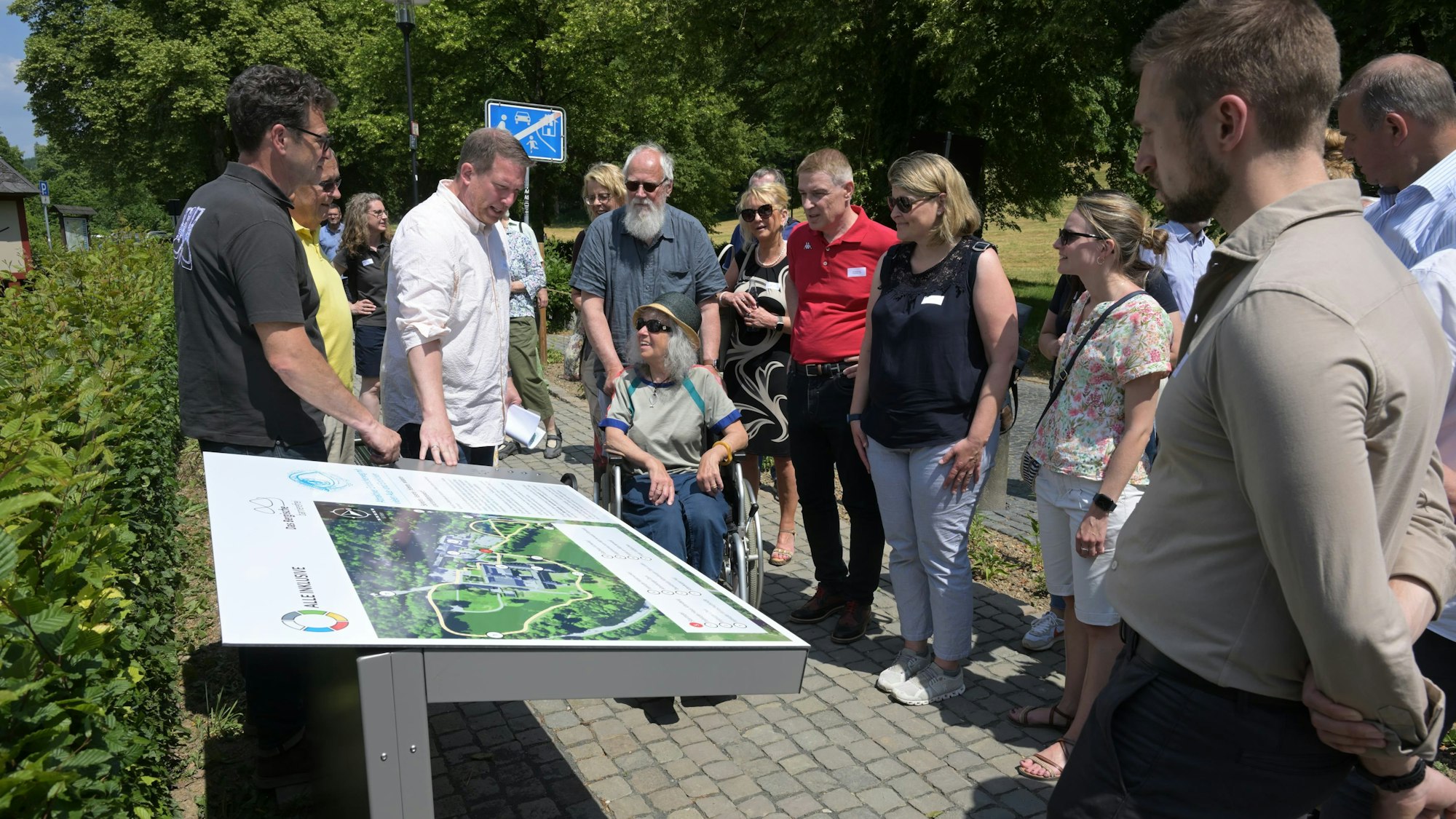 Menschen im Rollstuhl und ohne blicken auf eine Infotafel.