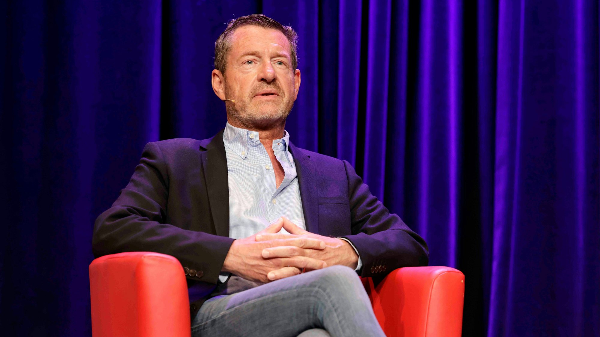 Kai Diekmann sitzt in einem roten Sessel auf der Bühne in der Comedia.