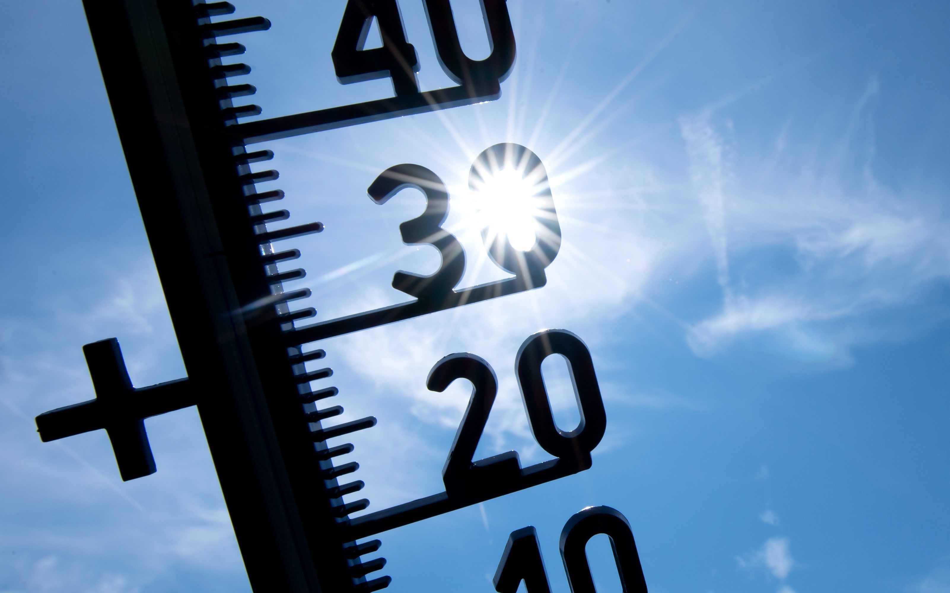 Blick auf ein Thermometer, im Hintergrund scheint die Sonne.