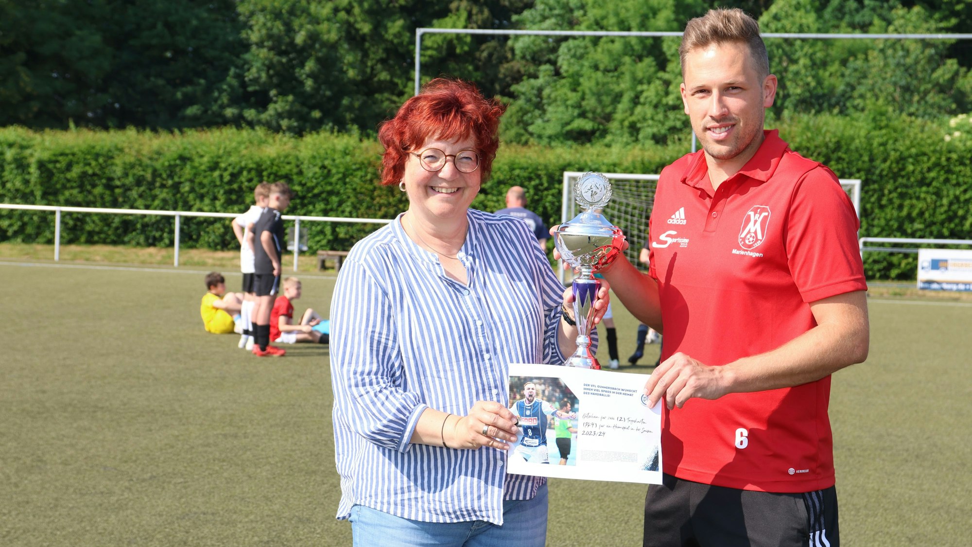 Eine Frau überreicht einem jungen Mann einen silbernen Pokal.