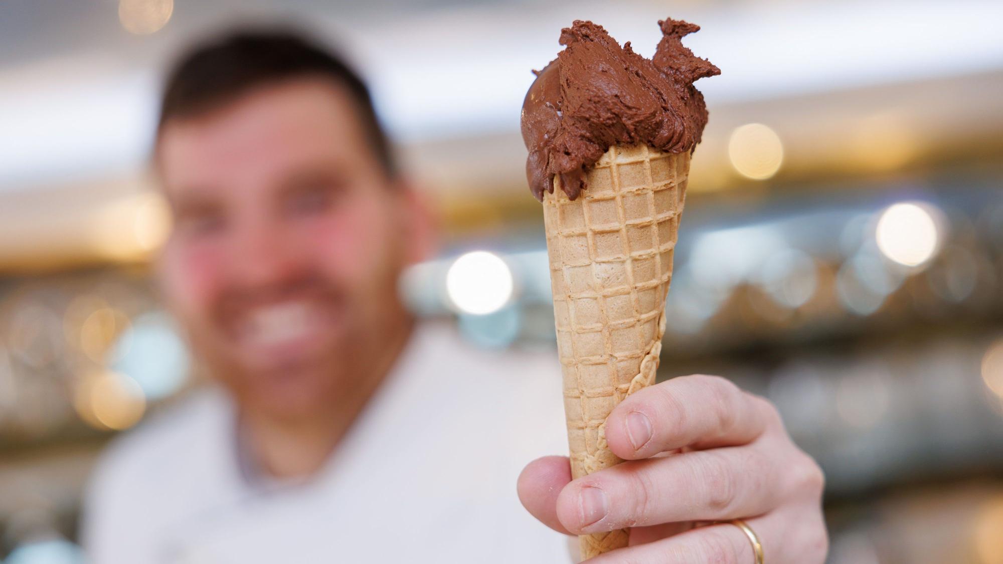 Ein Eisverkäufer hält eine Waffel mit einer Eiskugel Schokolade.