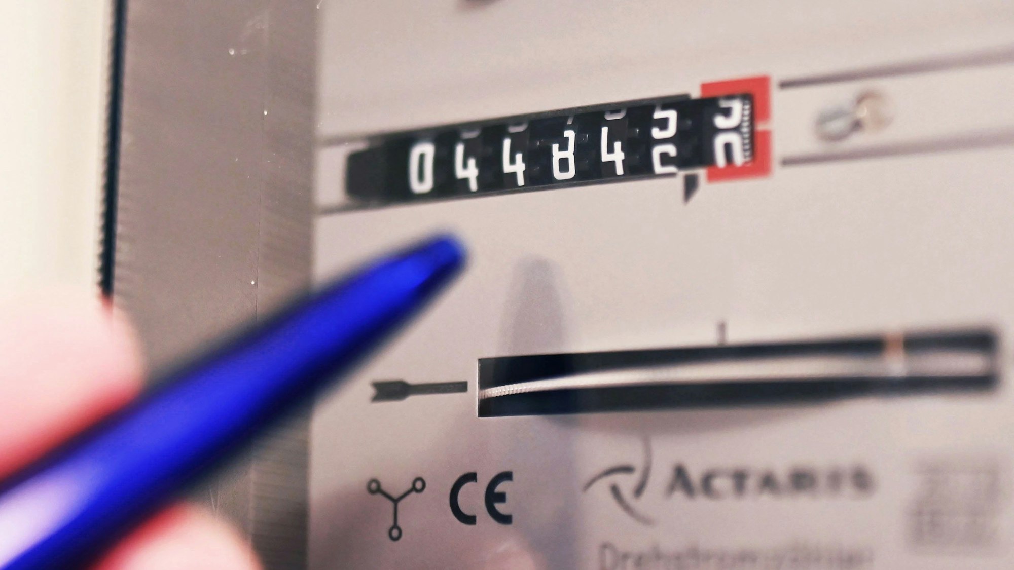 Ein Mensch tippt mit einem Kugelschreiber auf einen Stromzähler.