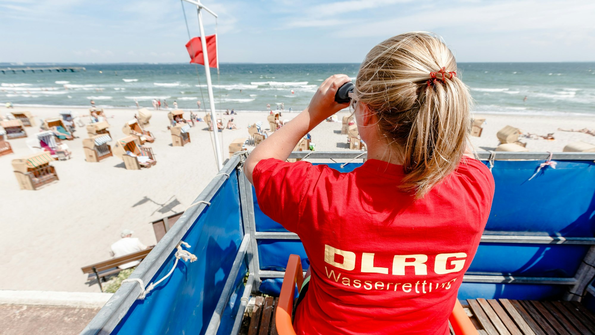 Eine Rettungsschwimmerin beobachtet den Timmendorfer Strand (Schleswig-Holstein). Ein 20-Jähriger ist bei einem Badeunfall ertrinken (Symbolbild)