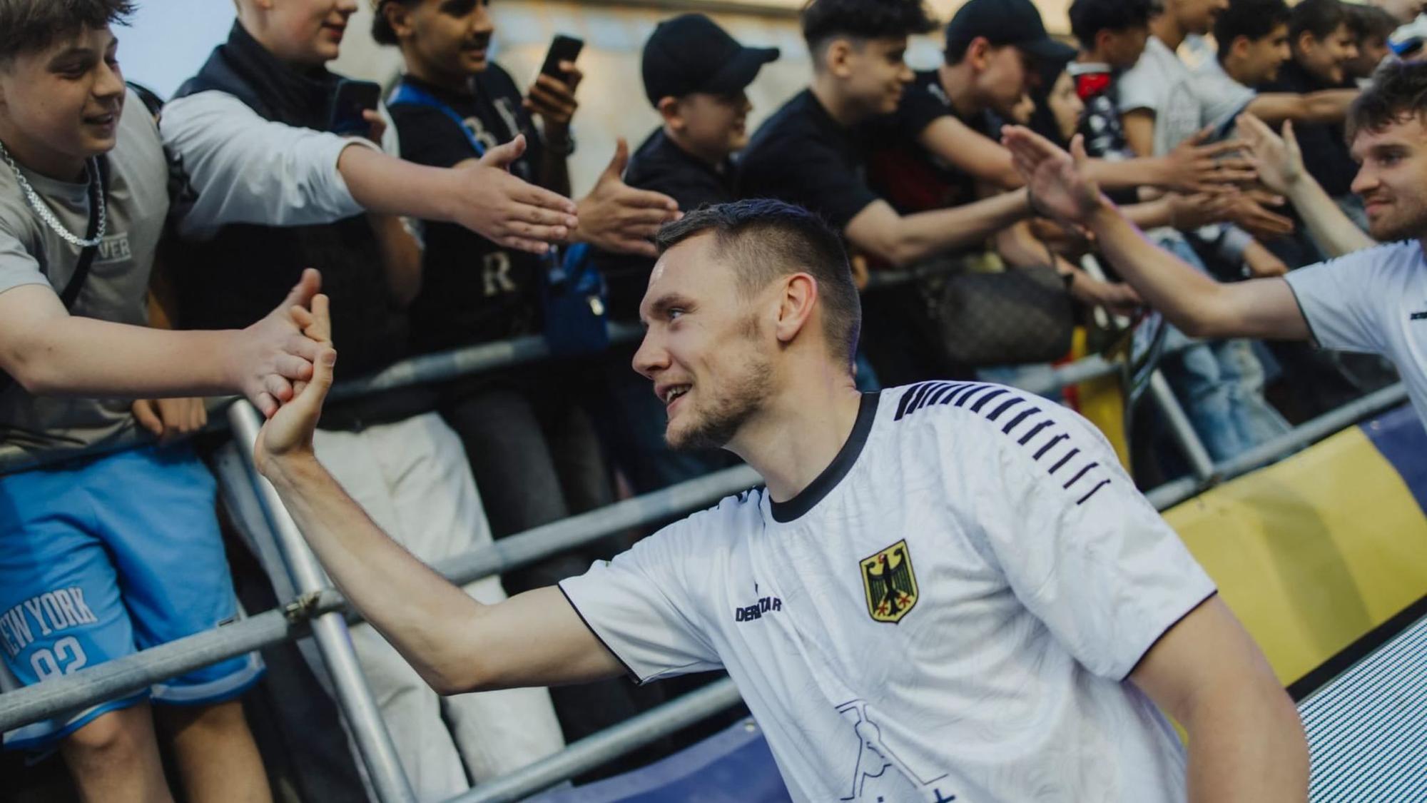 Ein Mann im deutschen Nationaltrikot schlägt mit Fans an einer Tribüne ab.