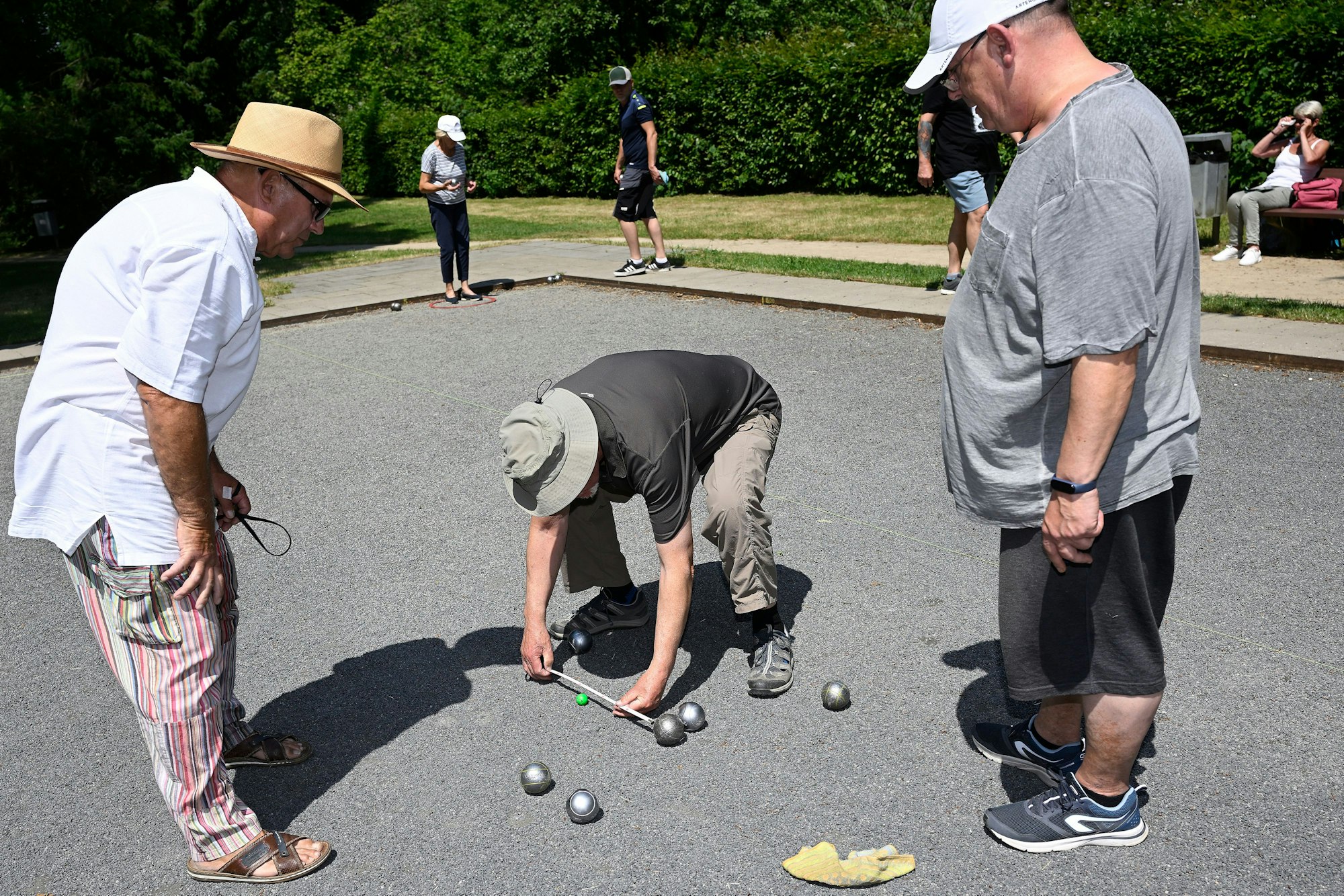 Ein Mann vermisst den Abstand einer Boule-Kugel zum „Schweinchen“.