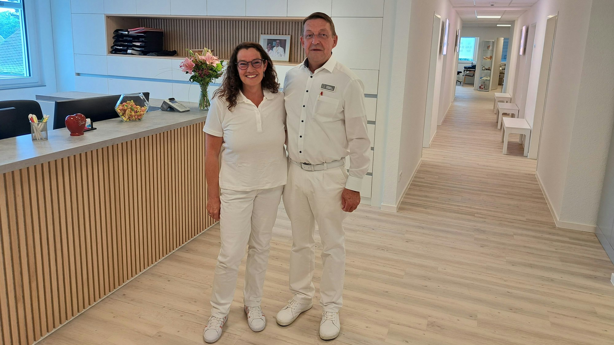 Ein weiß gekleidetes Paar steht dicht zusammen in dem Anmelderaum einer Praxis.