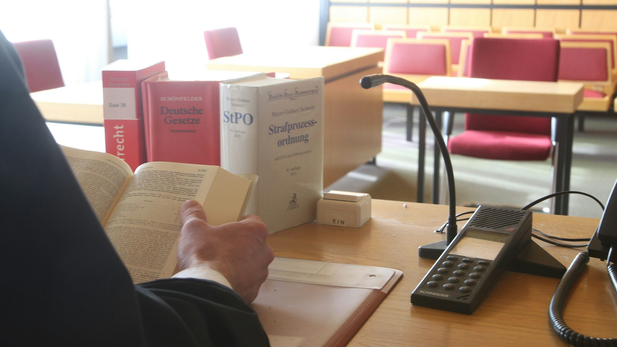 Ein Richter sitzt im Gerichtssaal vor einigen Gesetzbüchern.