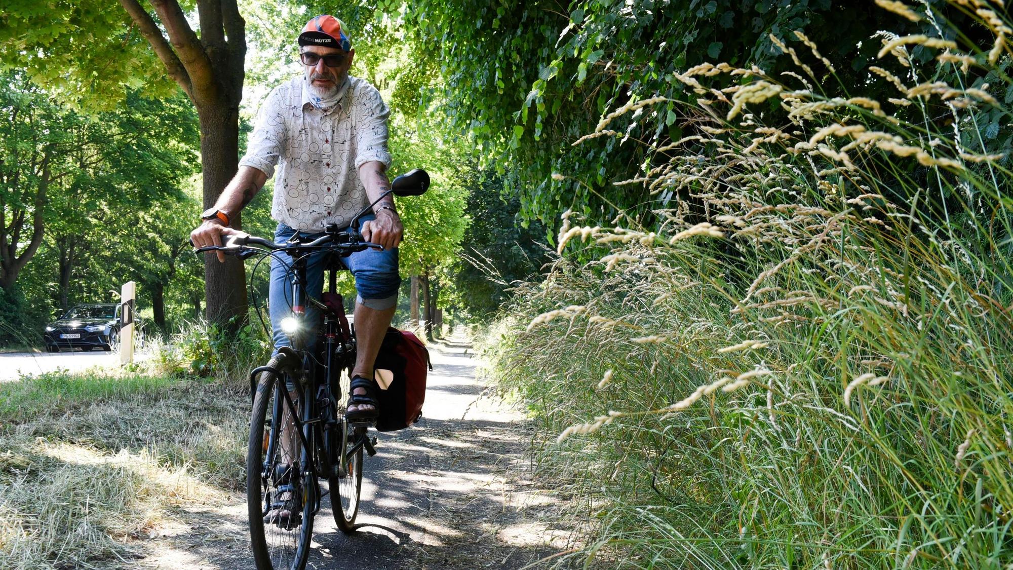 Das Foto zeigt Axel Fell auf dem Radweg an der Aachener Straße in Frechen. Gräser ragen in die Fahrbahn hinein.