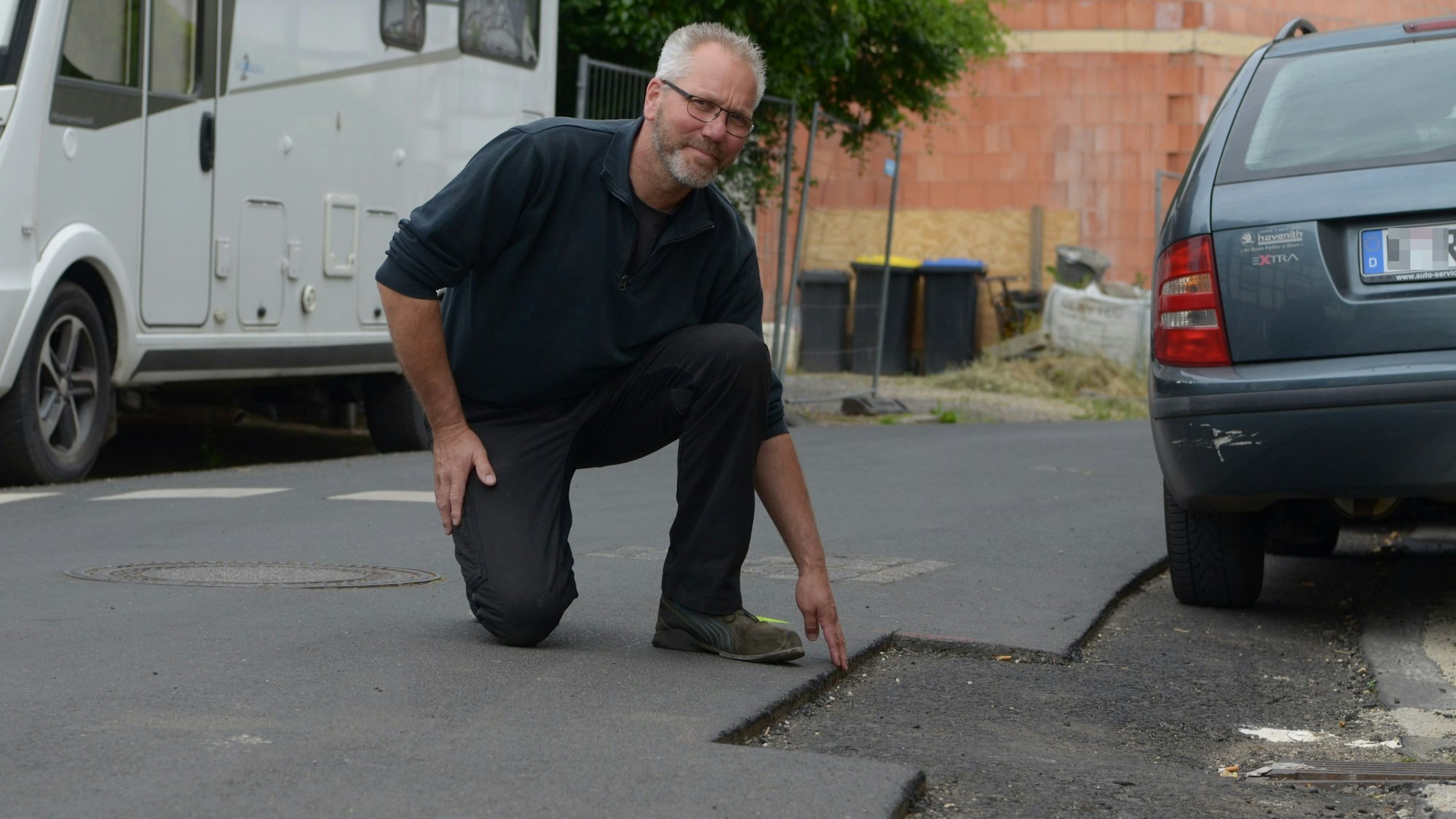 Ein Mann kniet an einer Fräskante in einer Straße, die eine Gefahrenquelle für Radfahrer sein kann.