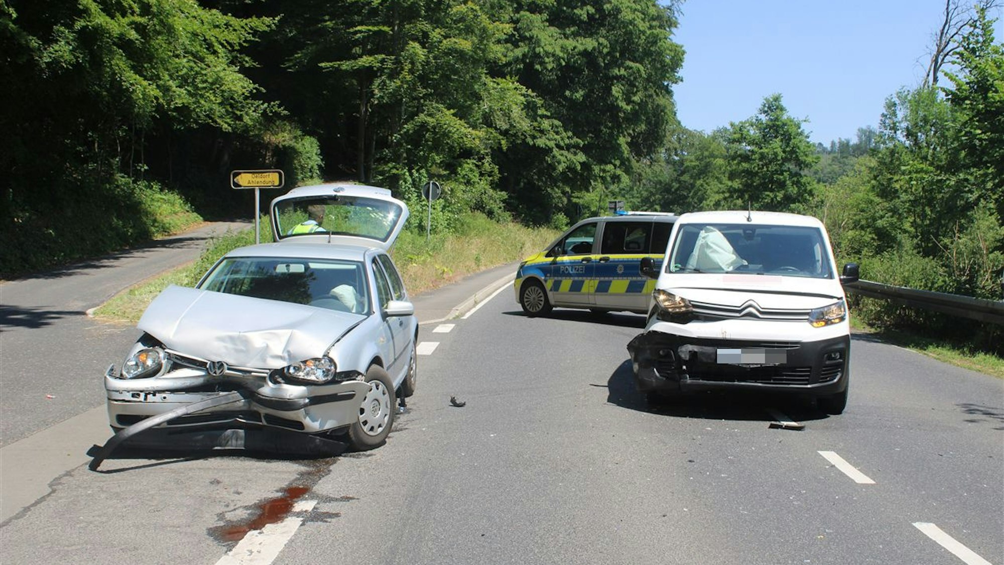 Zwei schwer beschädigte Autos stehen auf einer zweispurigen Straße, dahint steht ein Polizeifahrzeug.