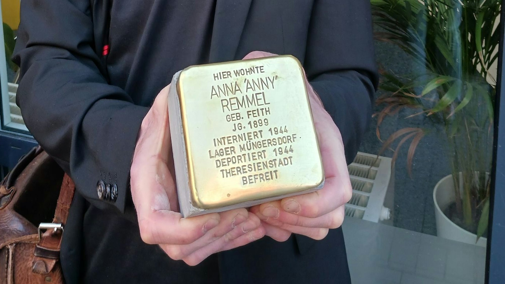 Ein Mann hält einen Pflasterstein, der mit einer goldfarbene Kappe und eingraviertem Text versehen ist.