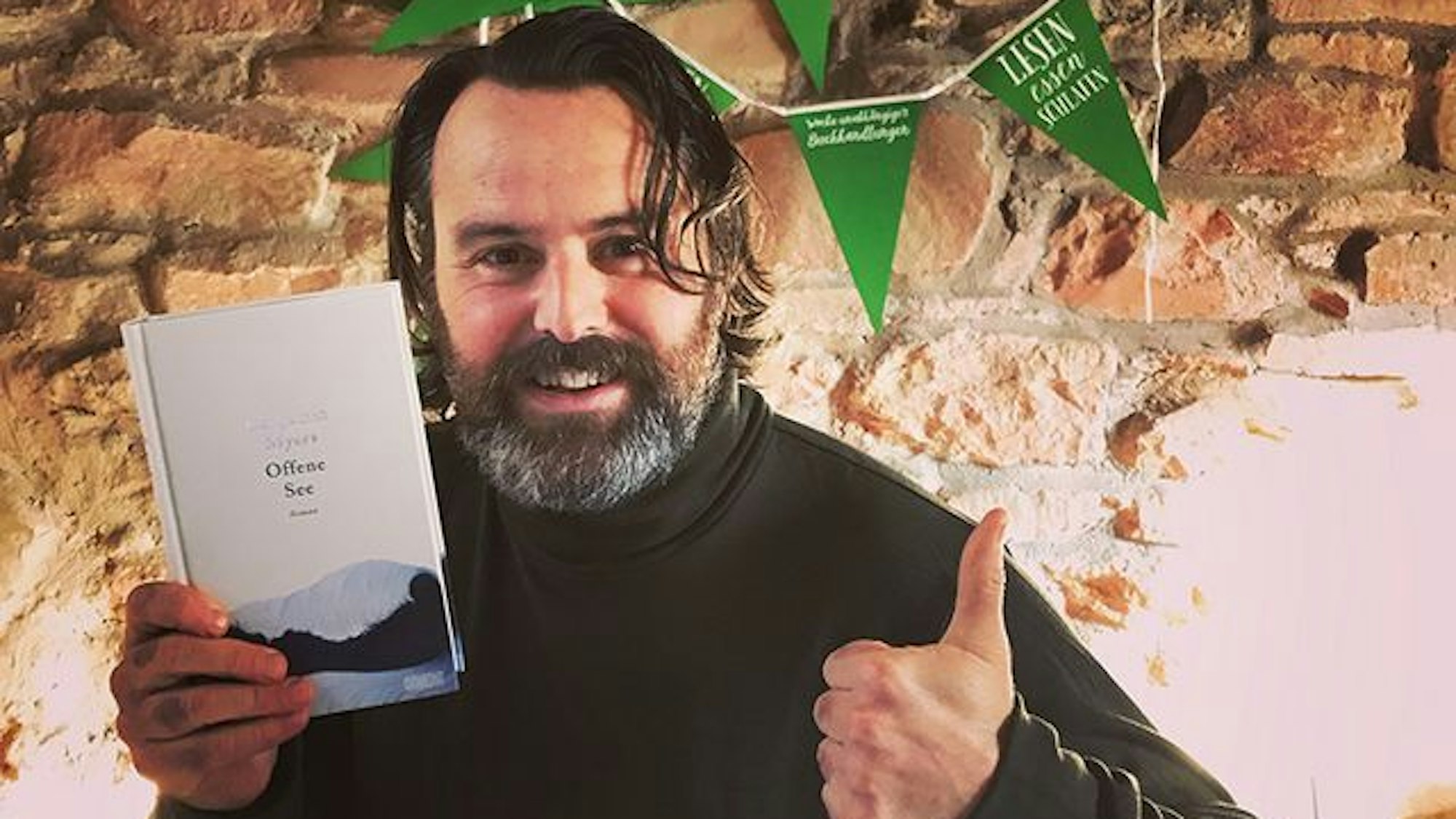 Auf dem Foto ist der Schriftsteller Benjamin Myers mit seinem Roman „Offene See“ zu sehen.