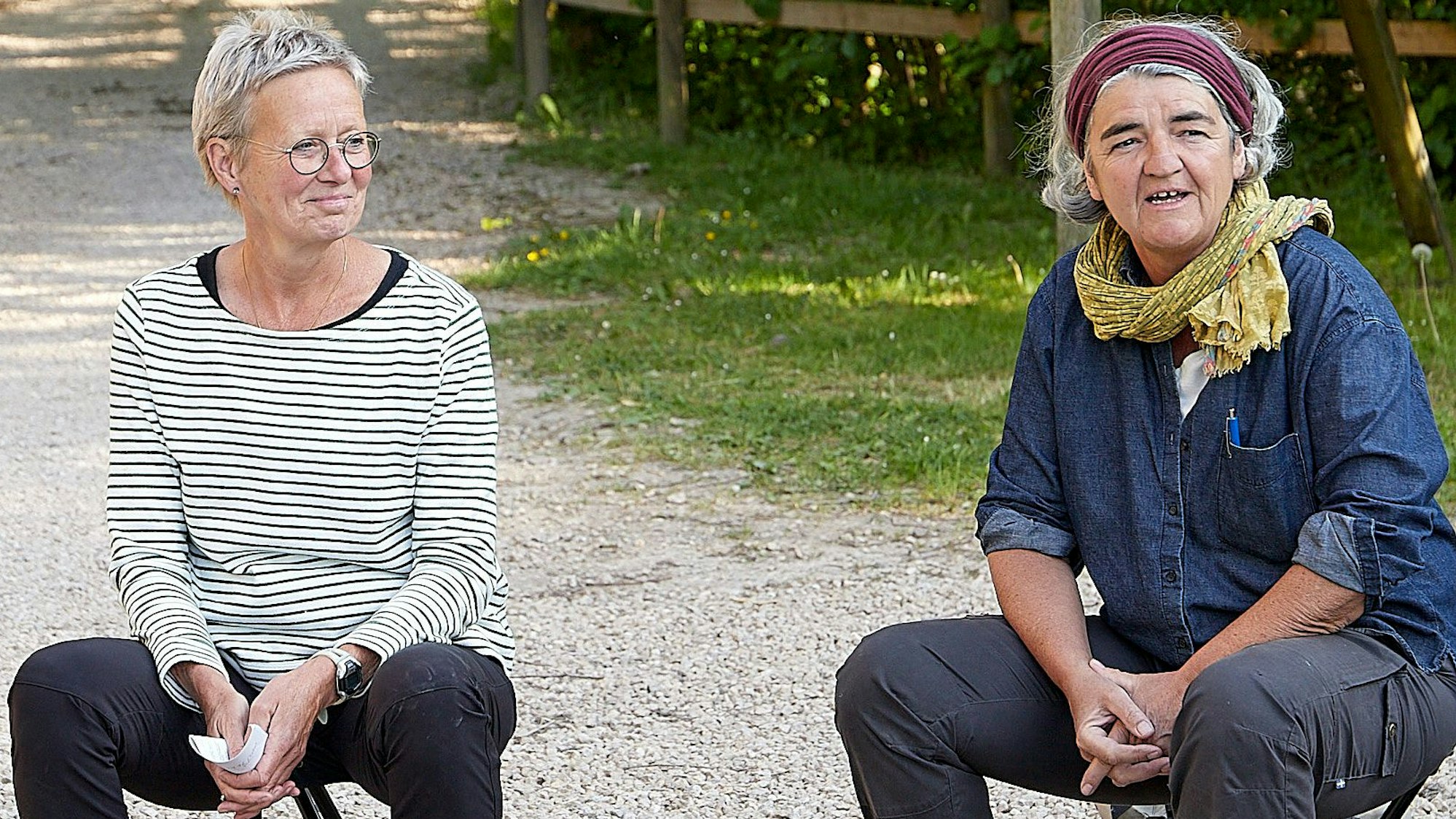 Die zwei Frauen Heidrun Grote und Ulrike Keuer sitzen auf ausklappbaren Hockern an einer Weggabelung in der Eifeler Natur.