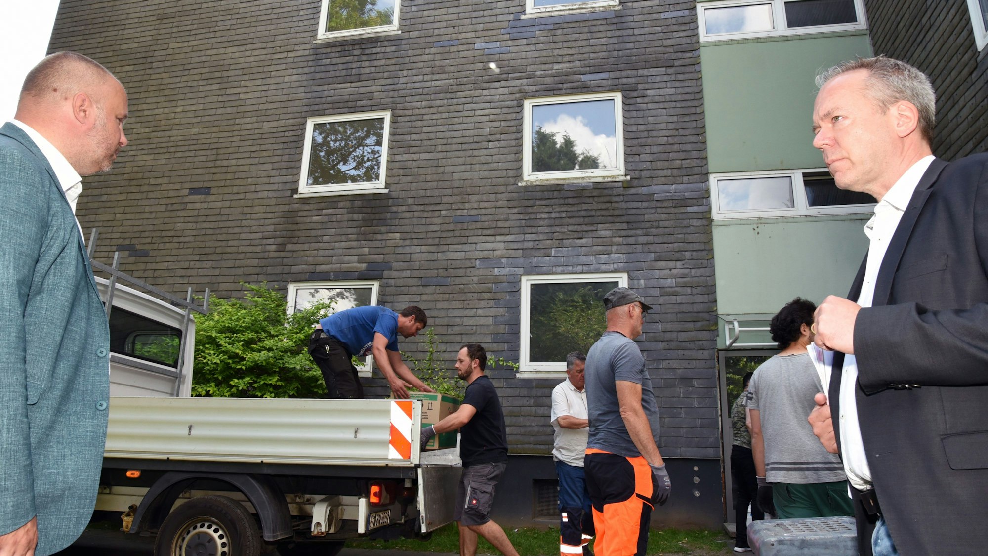 Zwei Männer stehen vor einer Immobilie, die geräumt wurde. Im Hintergrund sind Arbeiter im Einsatz zu sehen.