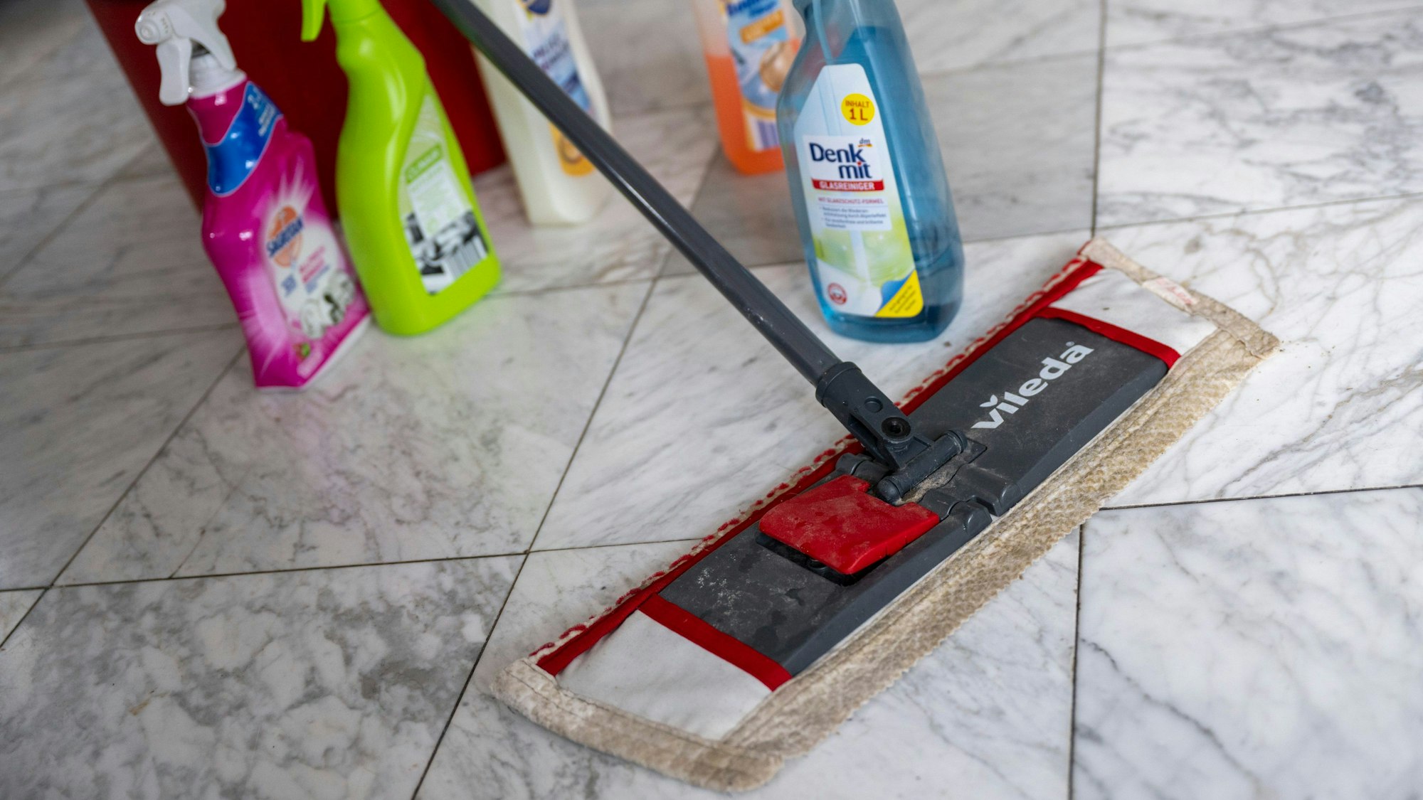 Ein Wischmopp und diverse Putzmittel stehen auf dem Boden.
