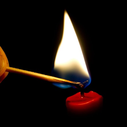 Auf dem Foto ist zu sehen, wie jemand mit einem Streichholz eine Kerze anzündet.