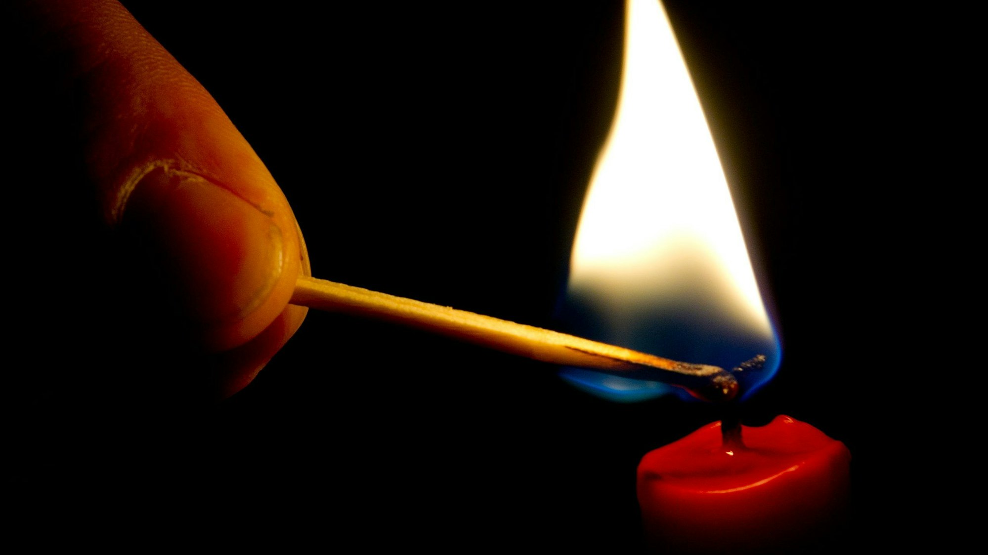 Auf dem Foto ist zu sehen, wie jemand mit einem Streichholz eine Kerze anzündet.