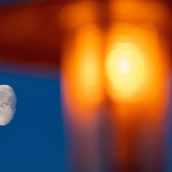 Der Mond ist am frühen Morgen neben einer Straßenlaterne am Himmel zu sehen.