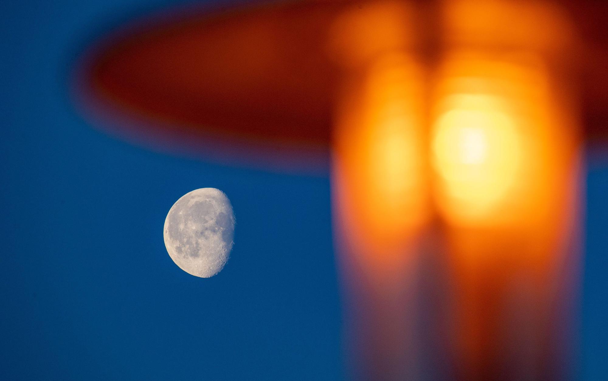 Der Mond ist am frühen Morgen neben einer Straßenlaterne am Himmel zu sehen.
