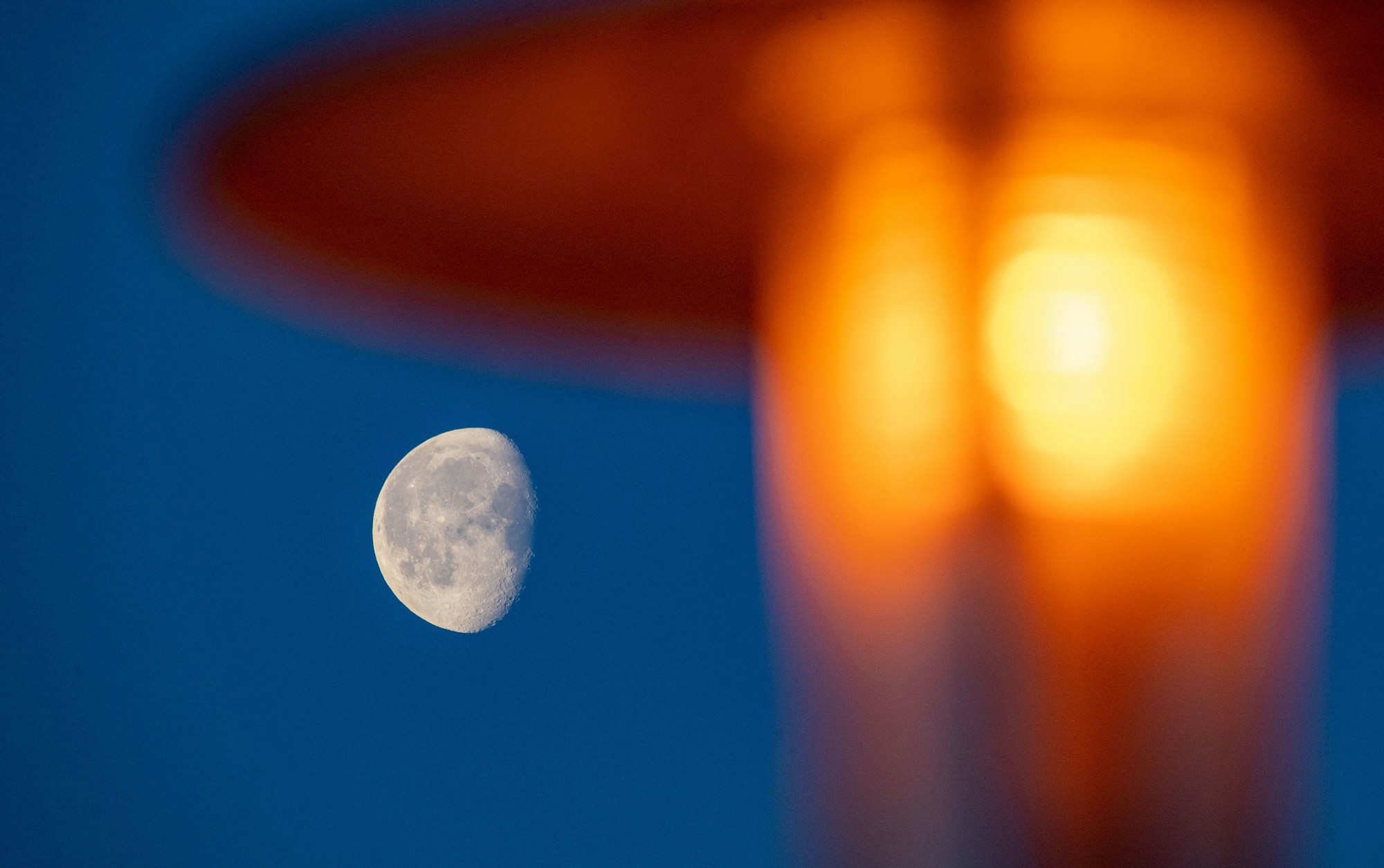 Der Mond ist am frühen Morgen neben einer Straßenlaterne am Himmel zu sehen.