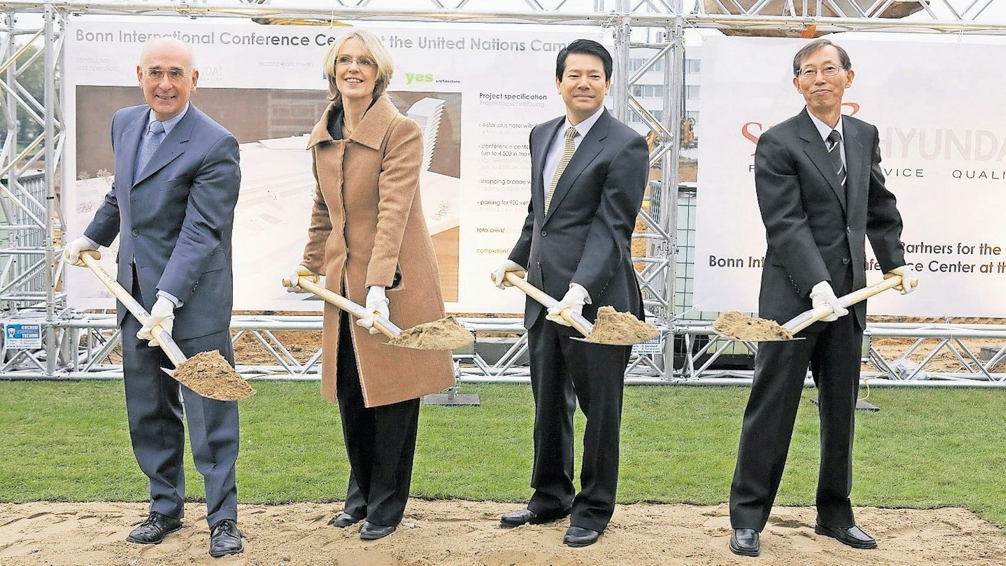Drei Männer und eine Frau stehen mit einem Spaten auf einer Wiese.