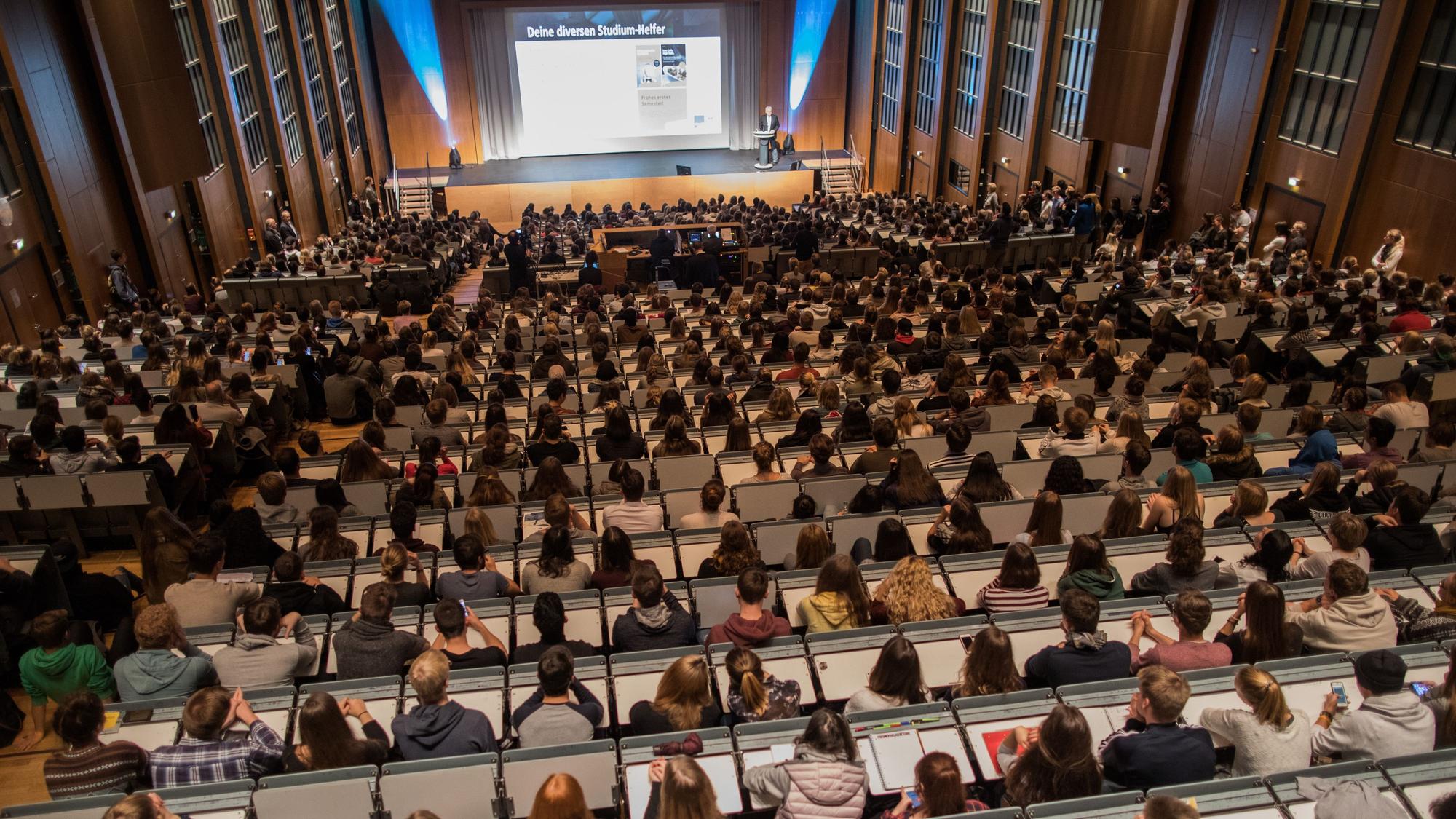 Studierende verfolgen im Hörsaal im Hauptgebäude der Universität zu Köln die Erstsemesterbegrüßung. Viele Studierende leben bei ihren Eltern.