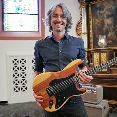 Ein Mann hält eine Gitarre in den Händen, die er aus dem Holz eines bei der Flutkatastrophe zerstörten Baums gebaut hat.