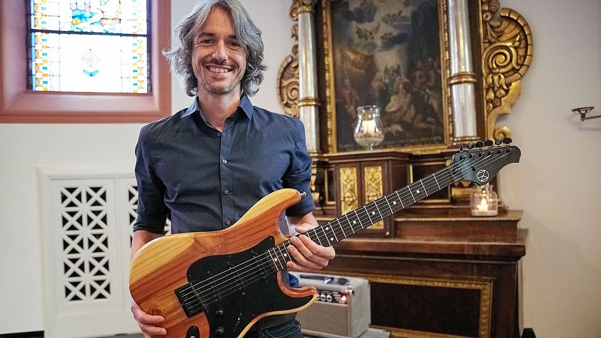 Ein Mann hält eine Gitarre in den Händen, die er aus dem Holz eines bei der Flutkatastrophe zerstörten Baums gebaut hat.