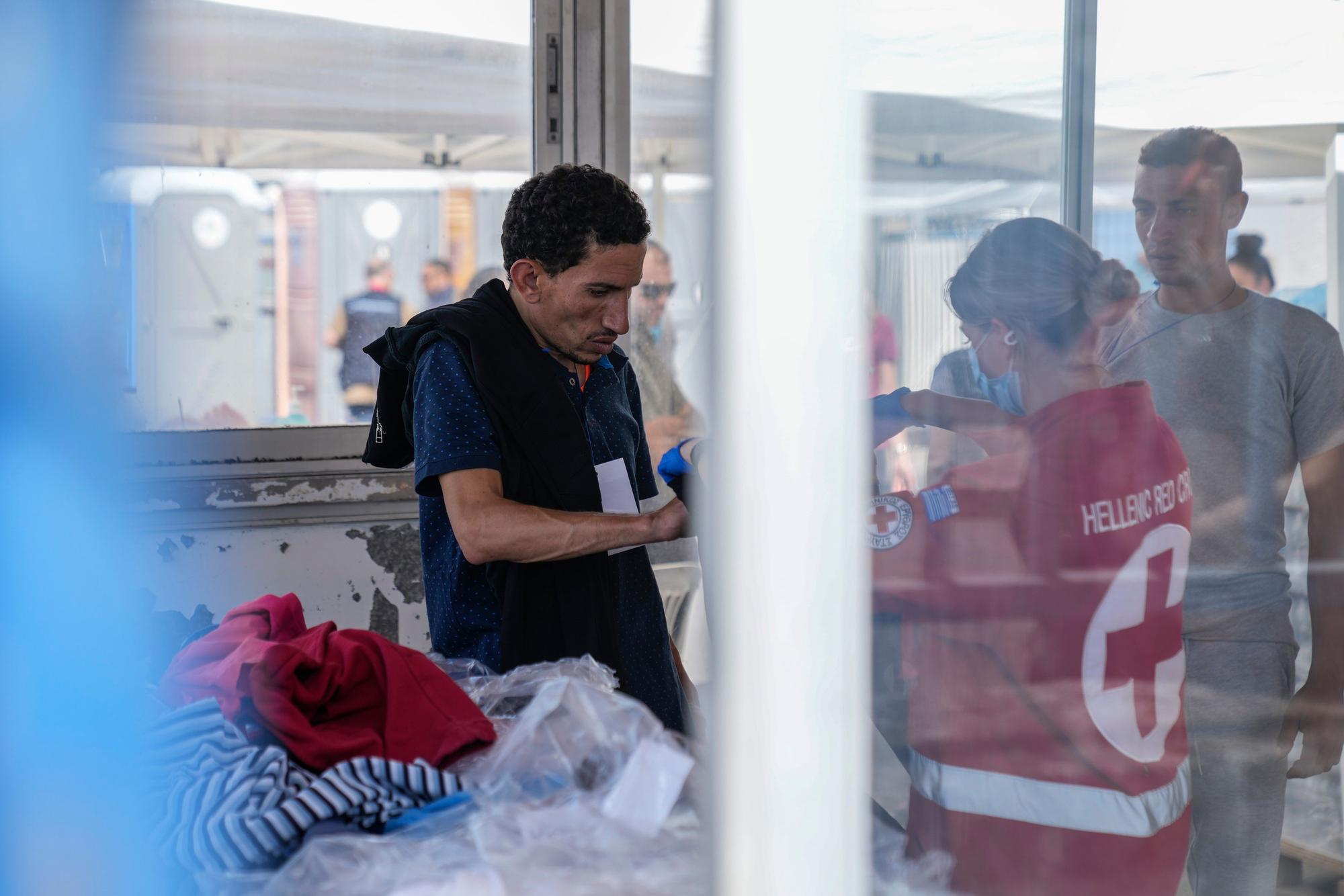 Eine Freiwillige des griechischen Roten Kreuzes gibt einem Überlebenden eines Bootsunglücks Kleidung vor einem Lagerhaus. Die 104 überlebenden Migranten eines Bootsunglücks vor Griechenland sollen am Donnerstag und Freitag in ein Flüchtlingslager nahe Athen gebracht werden. Zudem ist die Überführung der Toten nach Athen angelaufen, wie der Staatssender ERT berichtete. Dort sollen DNA-Proben genommen werden, um die Menschen zu identifizieren.