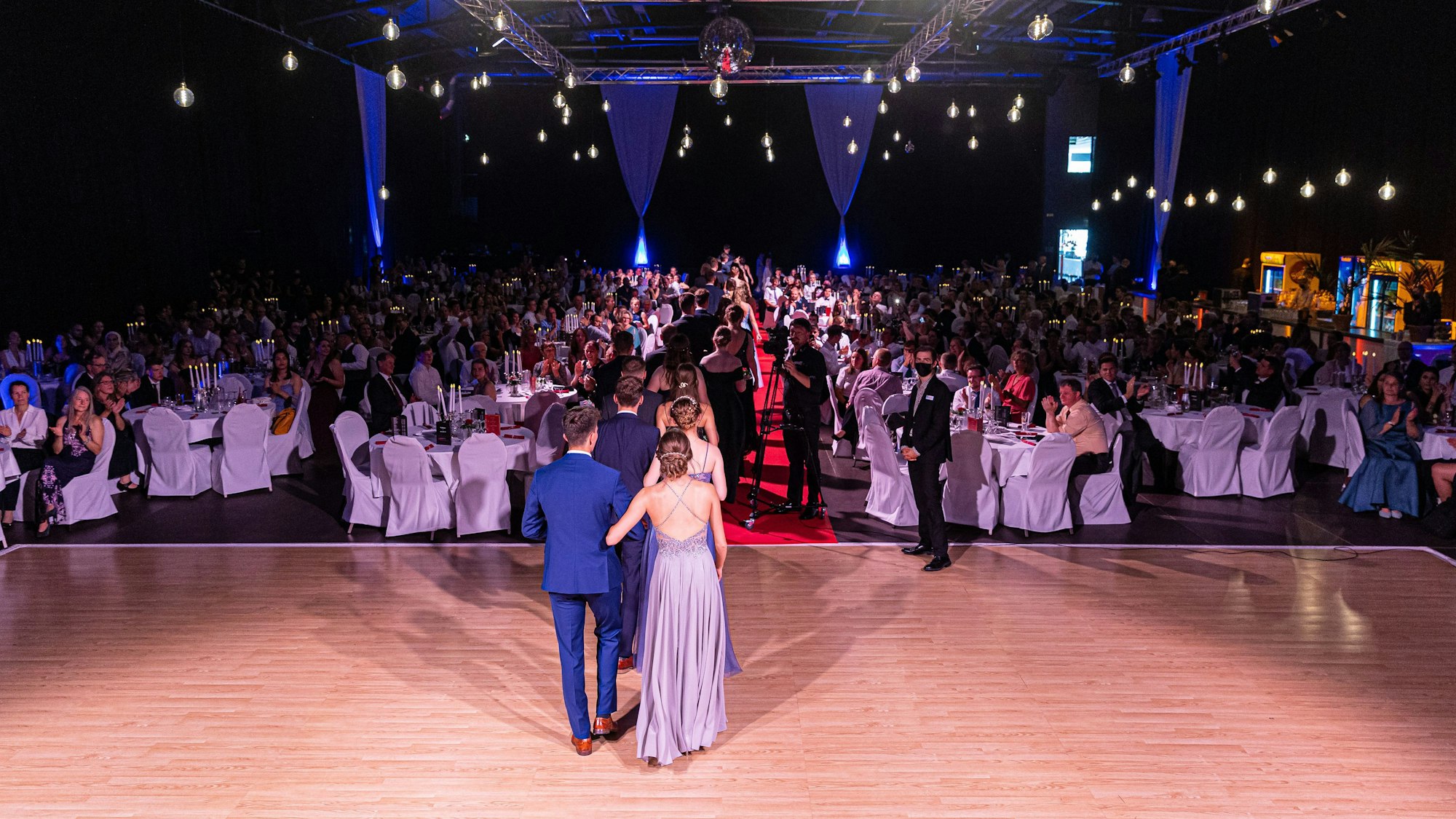 Schüler gehen Pärchenweise über einen roten Teppich.