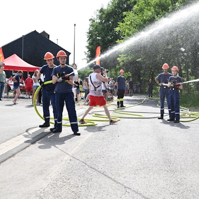 Mehrere junge Feuerwehrleute schießen Wasser aus zwei Schläuchen.