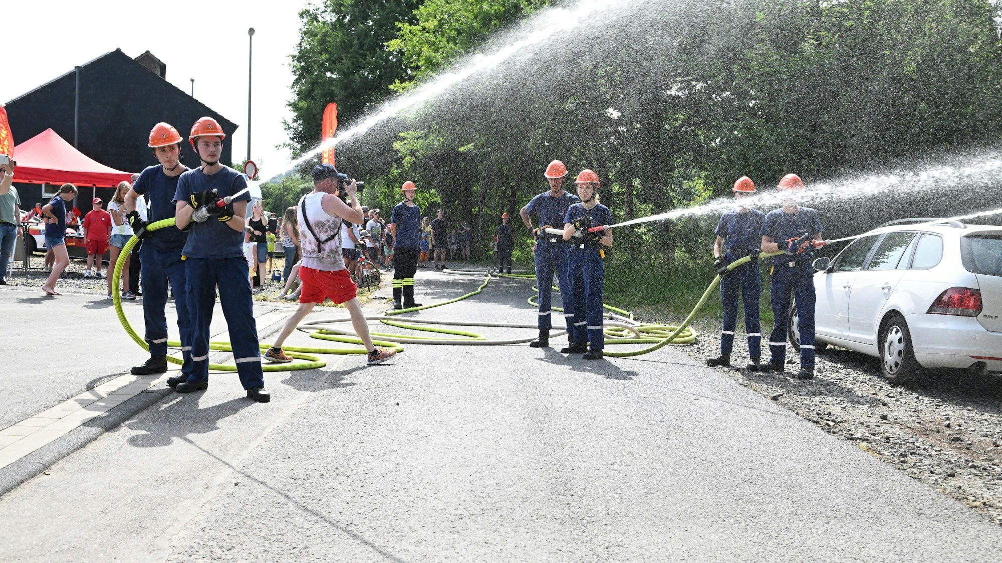 Mehrere junge Feuerwehrleute schießen Wasser aus zwei Schläuchen.