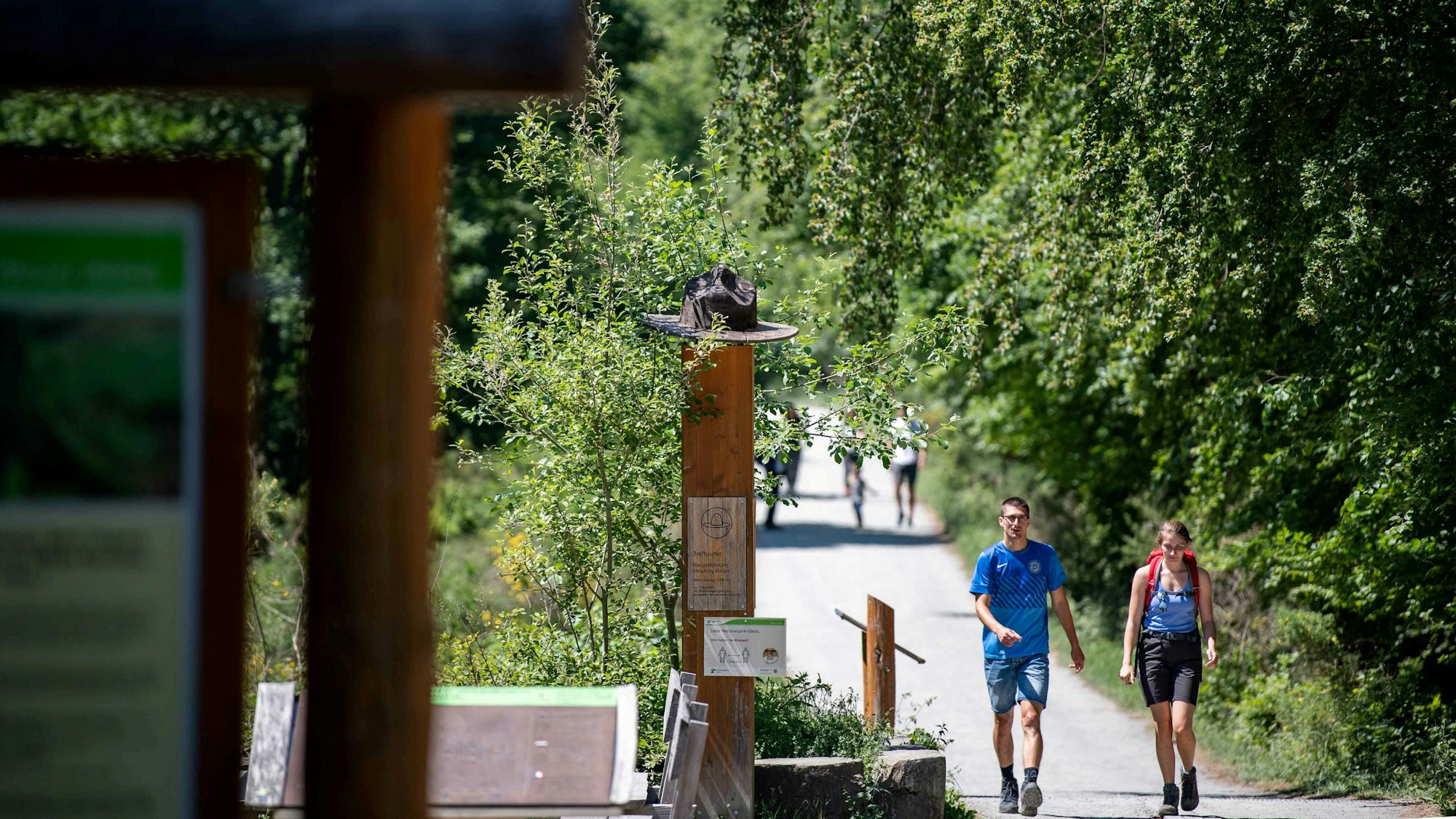 Wanderer laufen an einer Nationalparkstele mit Rangerhut vorbei.