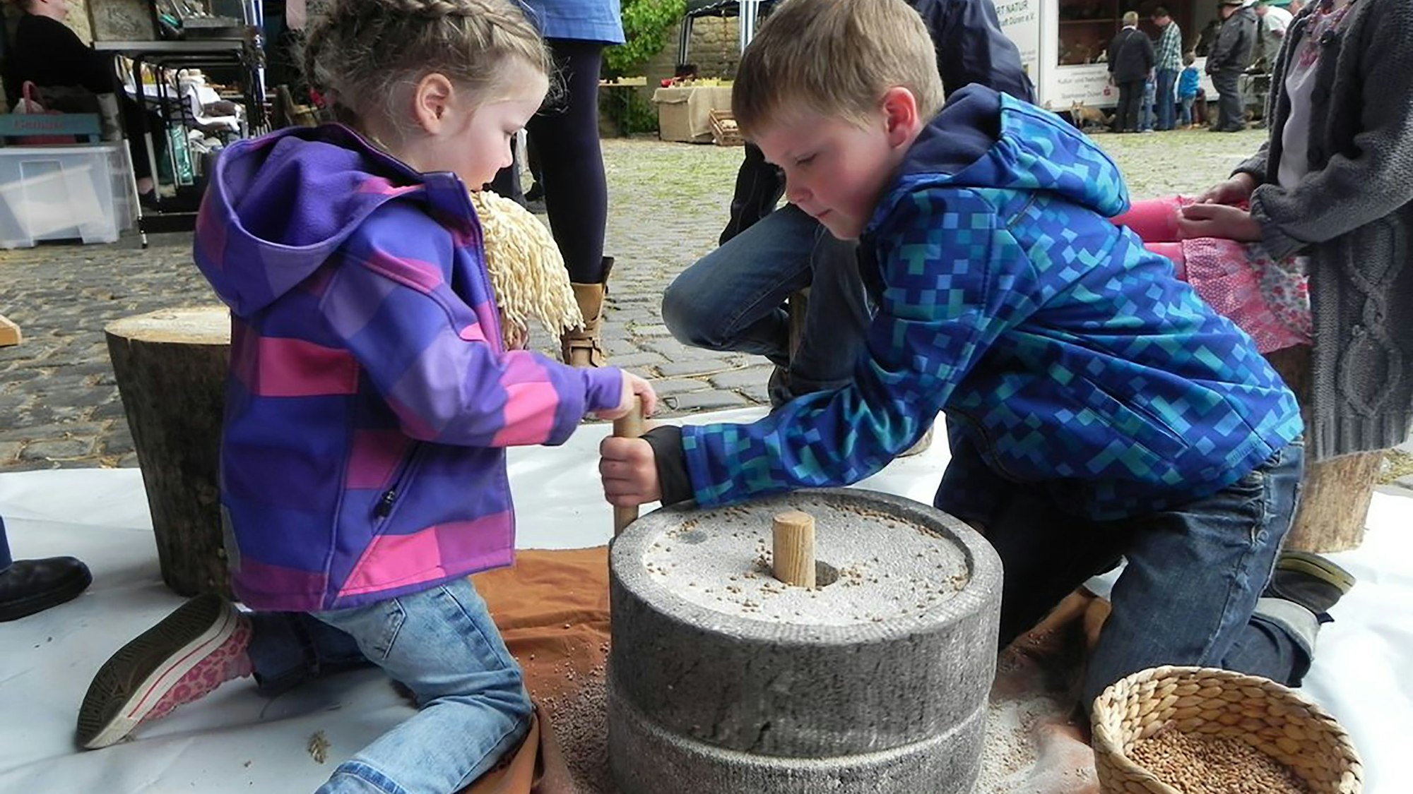 Zwei Kinder probieren eine römische Handmühle zum Mahlen von Getreide aus.