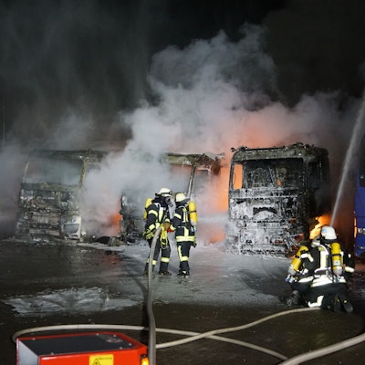 Das Bild zeigt sechs Feuerwehrleute, wie sie brennende Lkw löschen.