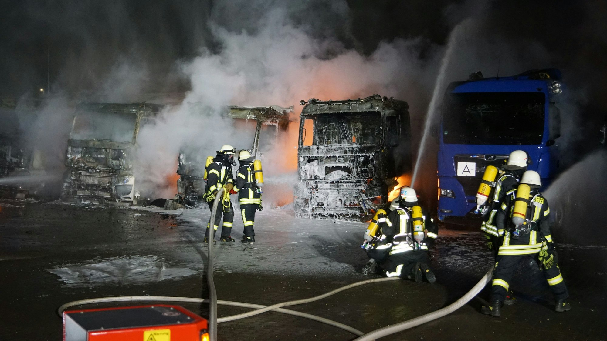 Das Bild zeigt sechs Feuerwehrleute, wie sie brennende Lkw löschen.