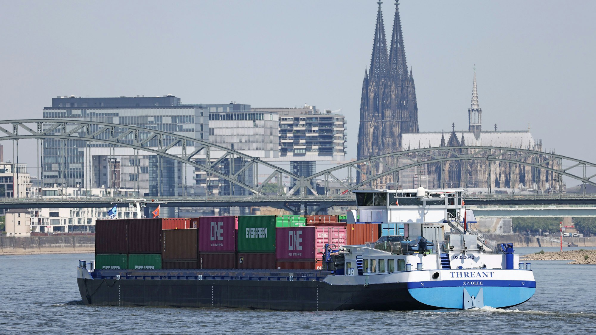Ein Binnenschiff, mit Containern beladen, fährt in Köln vor dem Dom (r) und den Kranhäusern (l) über den Rhein.