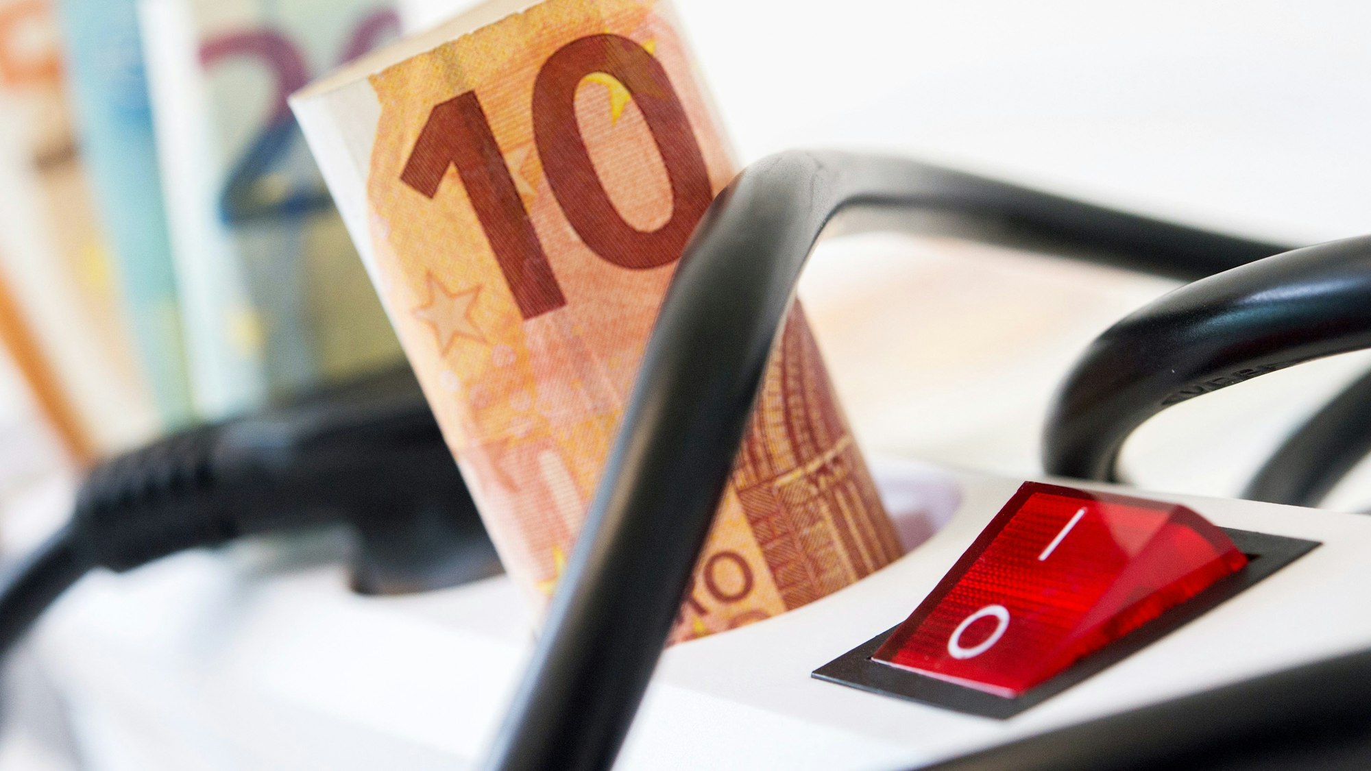 Die Strompreise sollen noch einmal deutlich steigen. Unser Symbolfoto zeigt Geldscheine in einer Steckerleiste.