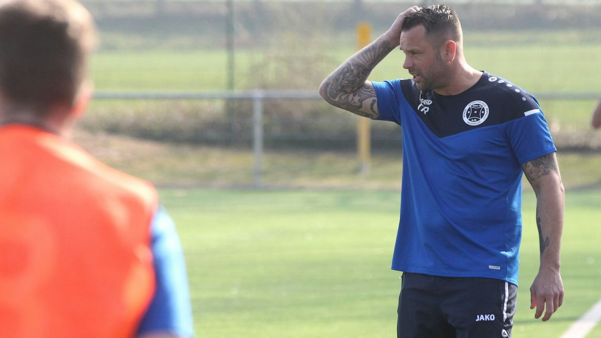 DHO-Trainer Gerrit Ueckert steht an der Seitenlinie, beobachtet das Spiel und fährt sich mit der rechten Hand durch die Haare.