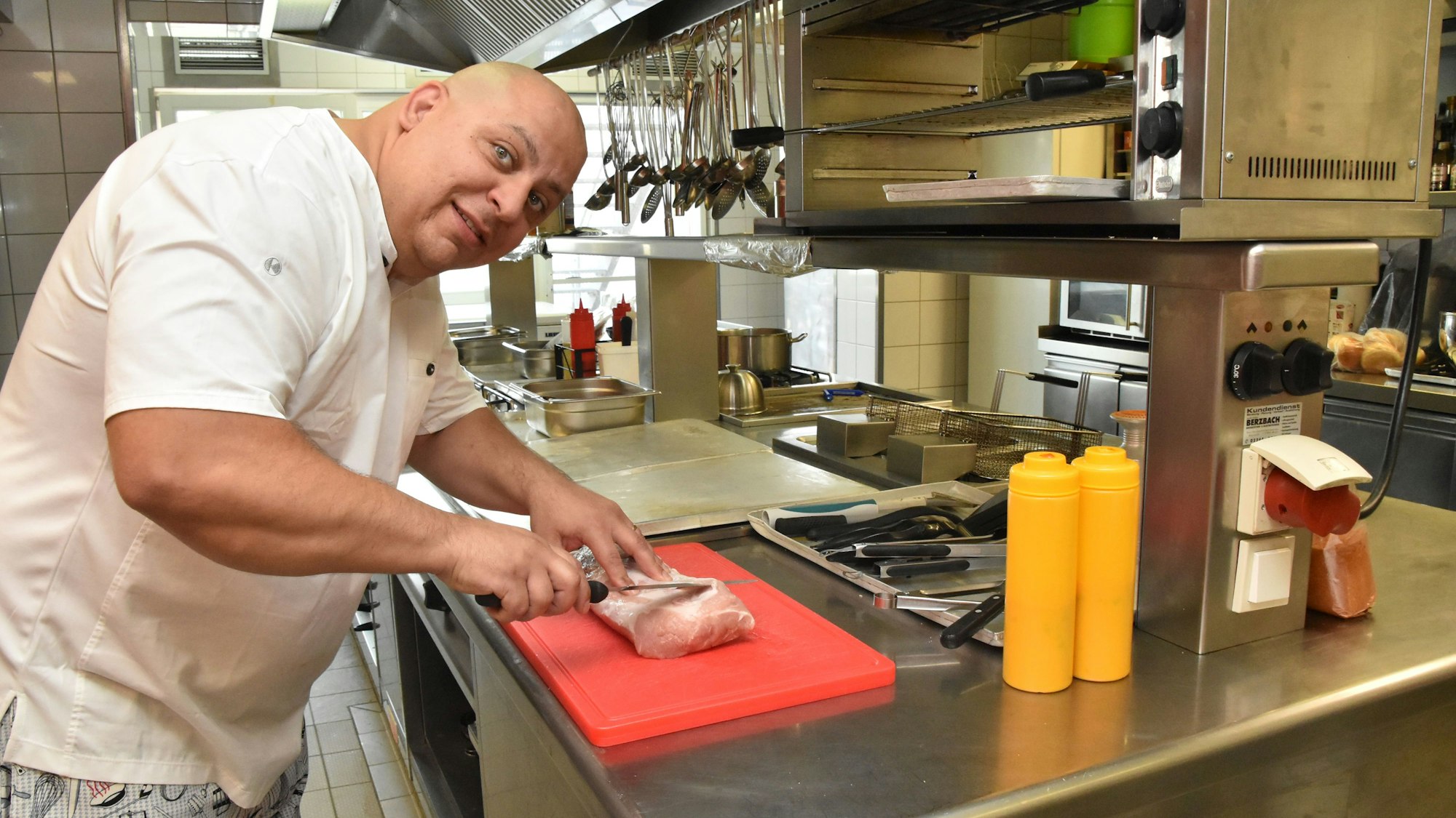 Der Koch steht in der Küche und schneidet ein Stück Schweinefleisch.