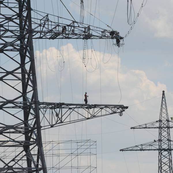 Das Foto zeigt einen Monteur auf einem Ausleger eines Hochspannungsmasten.