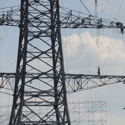 Das Foto zeigt einen Monteur auf einem Ausleger eines Hochspannungsmasten.