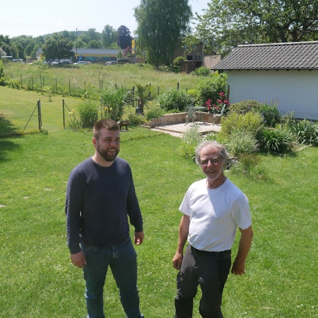 Luca Schwarzer und Ferdinand Patt stehen nebeneinander auf einer Wiese und lachen in die Kamera.
