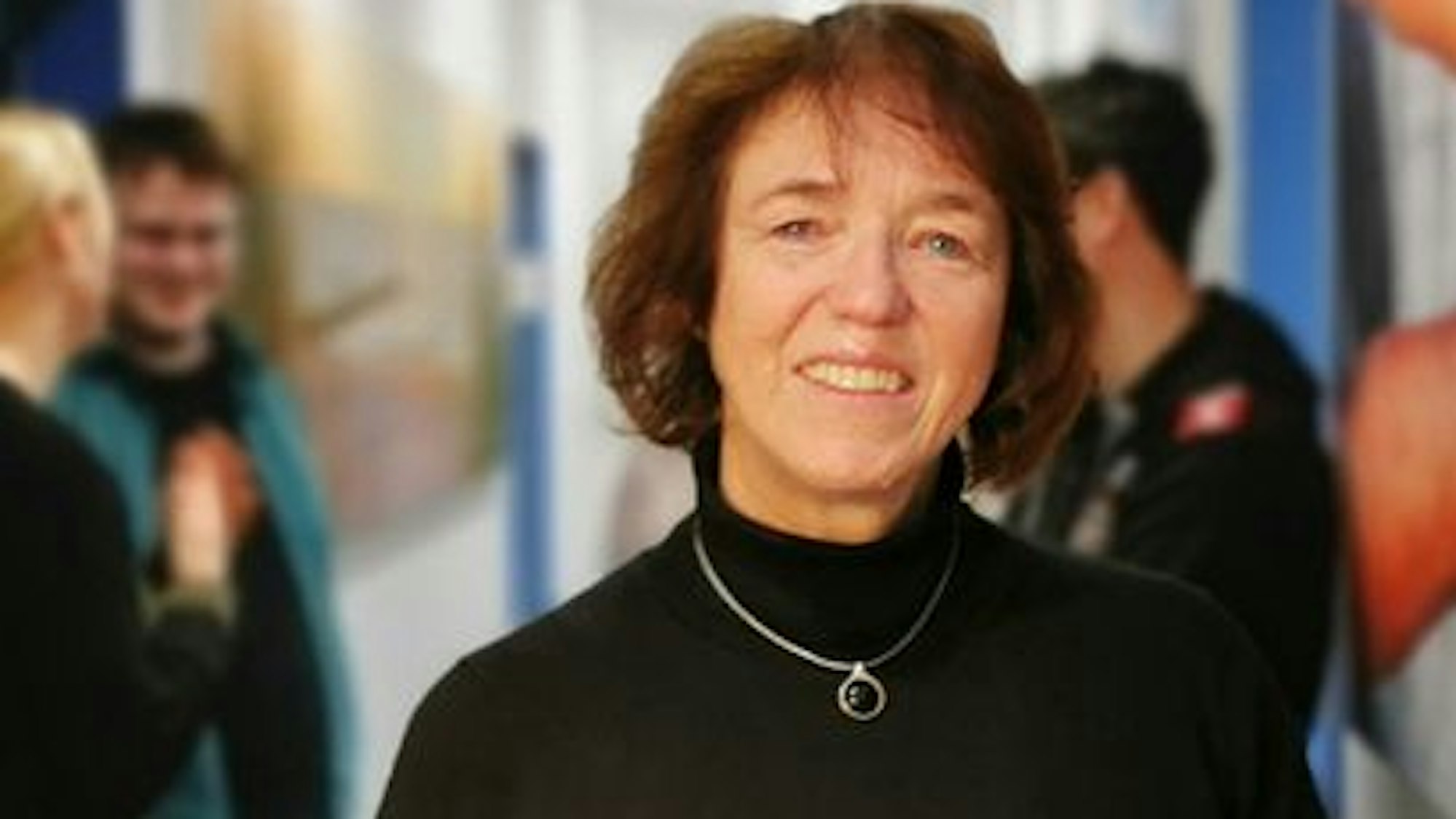 Eine Frau steht in einem Gang mit großen Bildern an den Wänden und Menschen im Hintergrund.