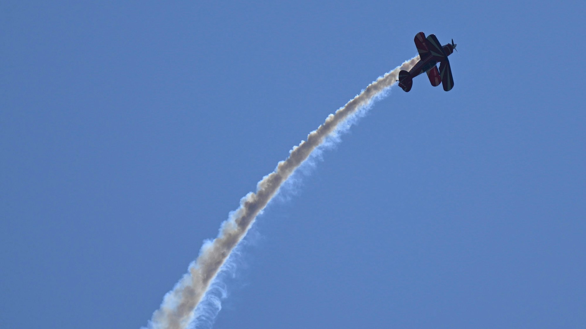 Ein Doppeldecker am Himmel zieht eine Nebelfahne hinter sich her.