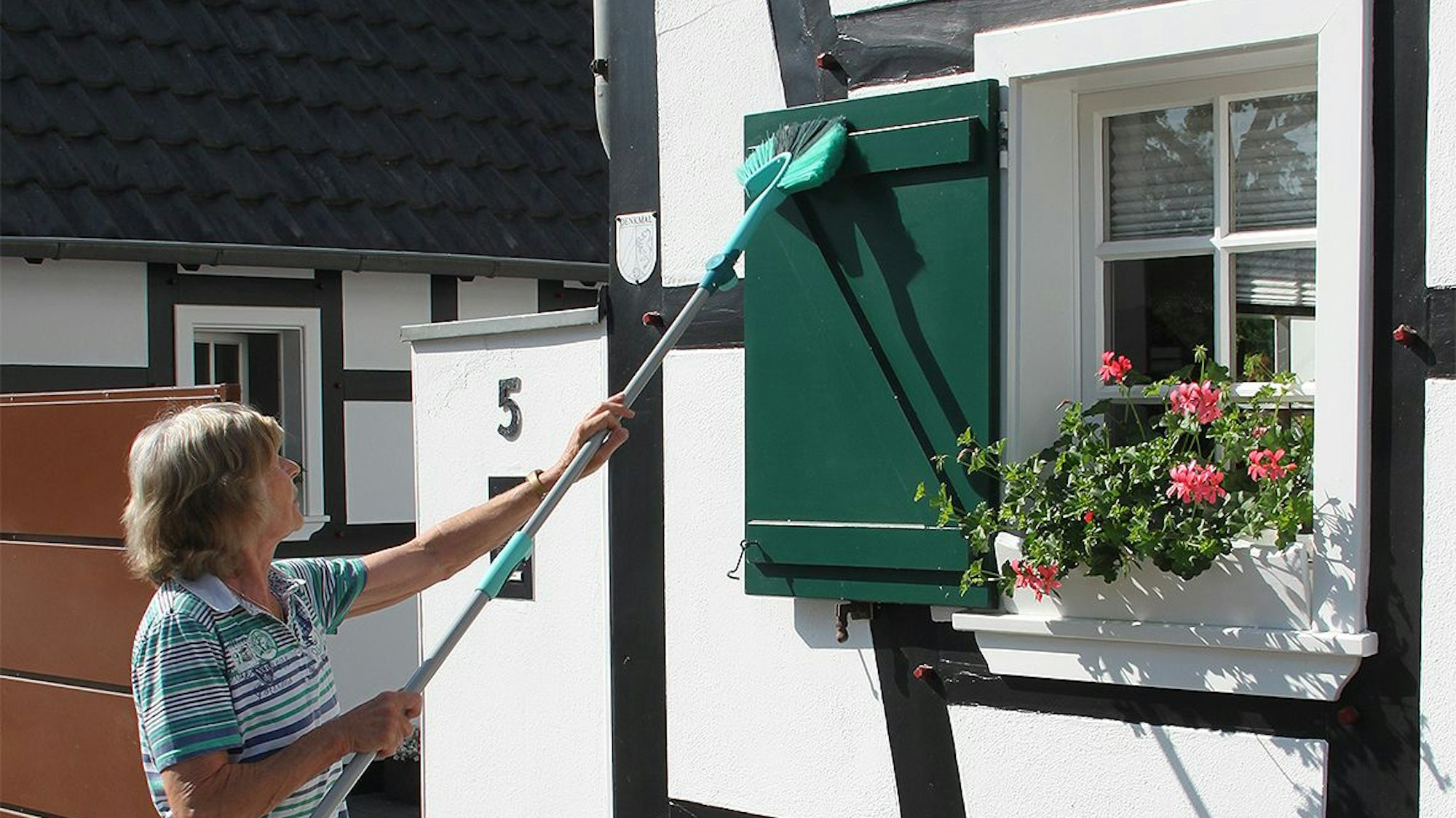 Eine Frau säubert die Fensterläden eines Fachwerkhauses.