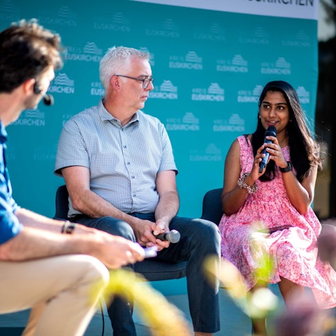 Zwei Männer und eine Frau diskutieren bei einer Podiumsveranstaltung.