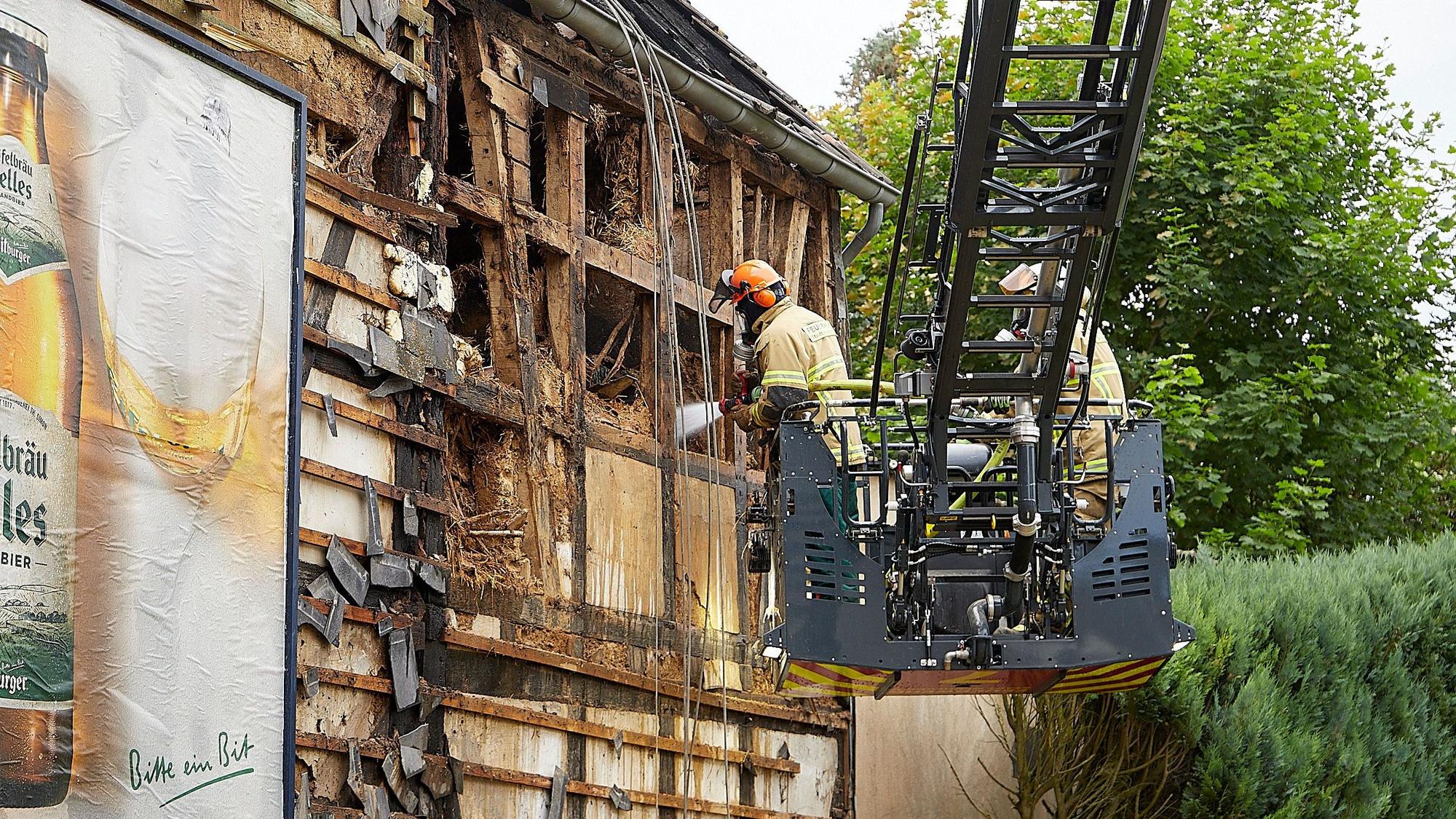 Das Bild zeigt zwei Feuerwehrleute, die vom Korb einer Drehleiter aus an einem Fachwerkhaus Löscharbeiten durchführen.