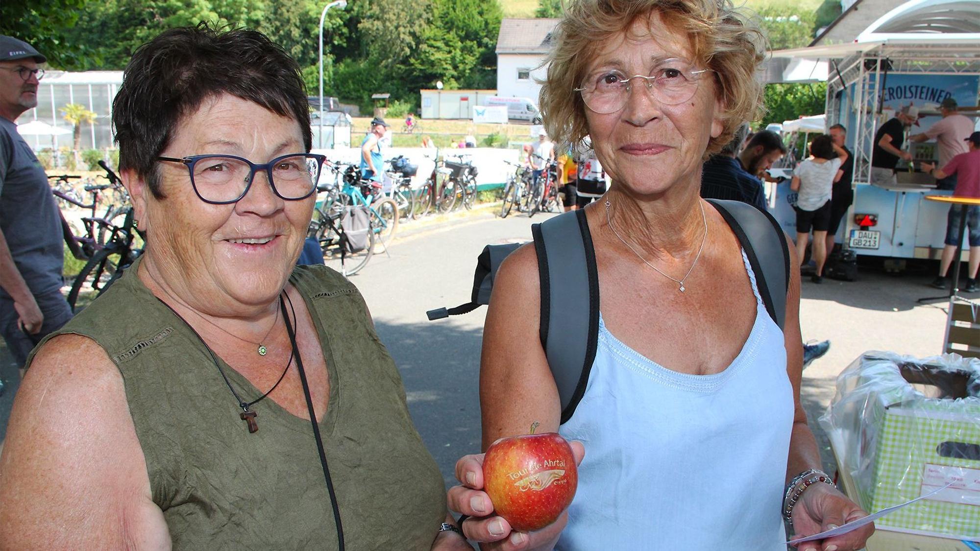 Das Bild zeigt zwei Frauen. Eine hält einen Apfel in der Hand, auf dem ein Logo aufgeprägt ist.